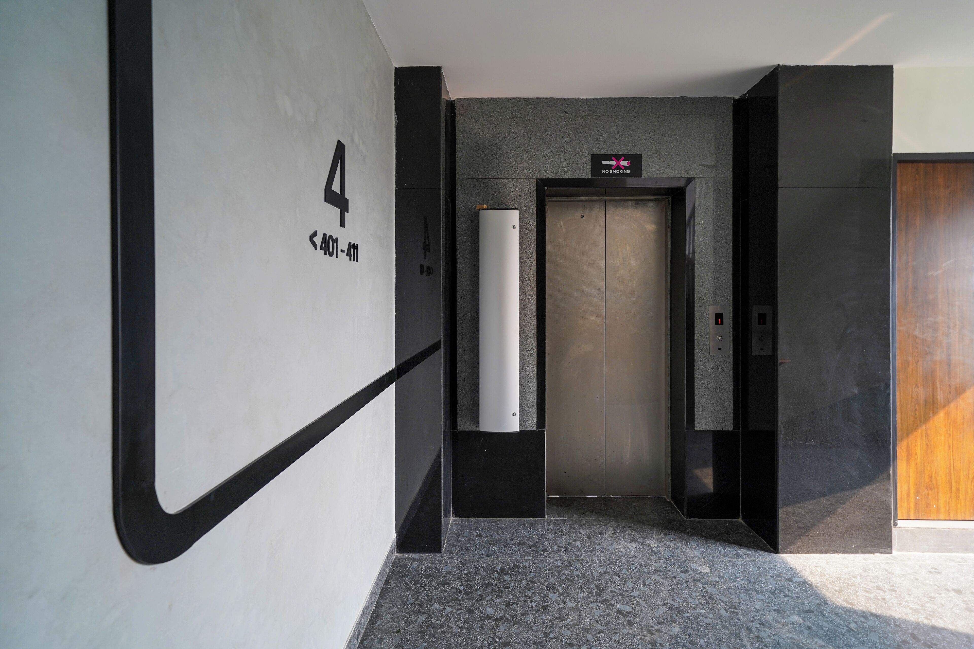 A modern hallway with a number '4' sign, an elevator, and a wooden door.
