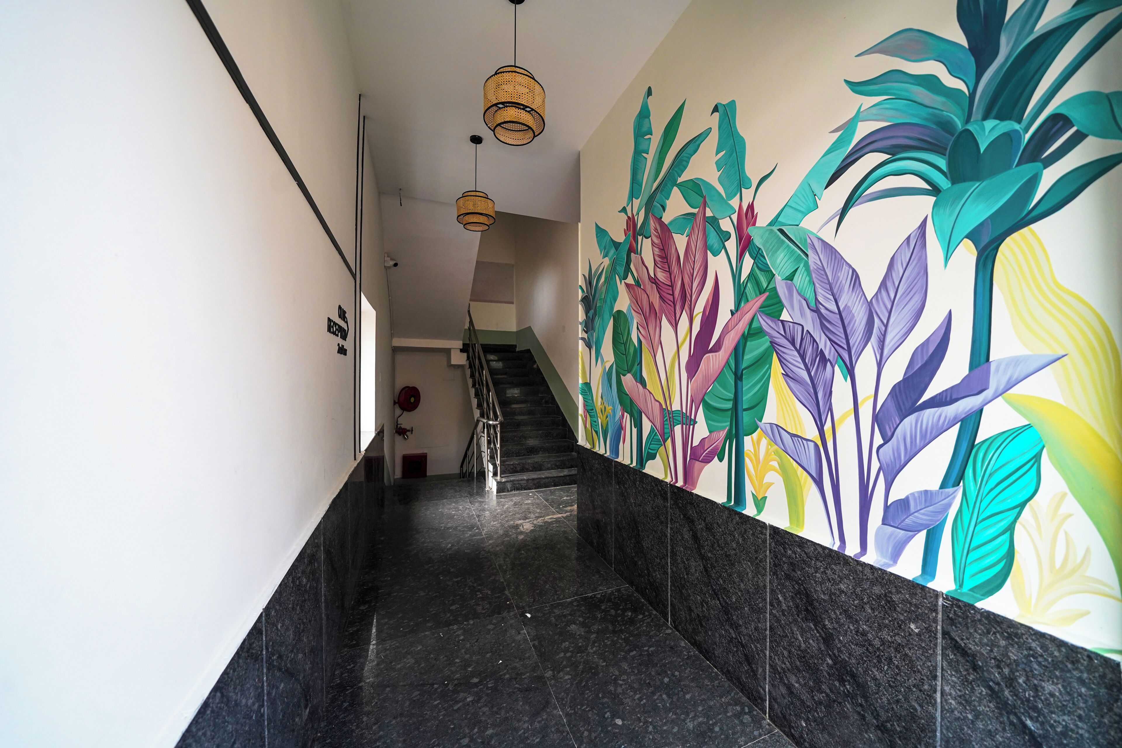 A hallway with a staircase, a wall mural with colorful plant designs, and a black marble floor.