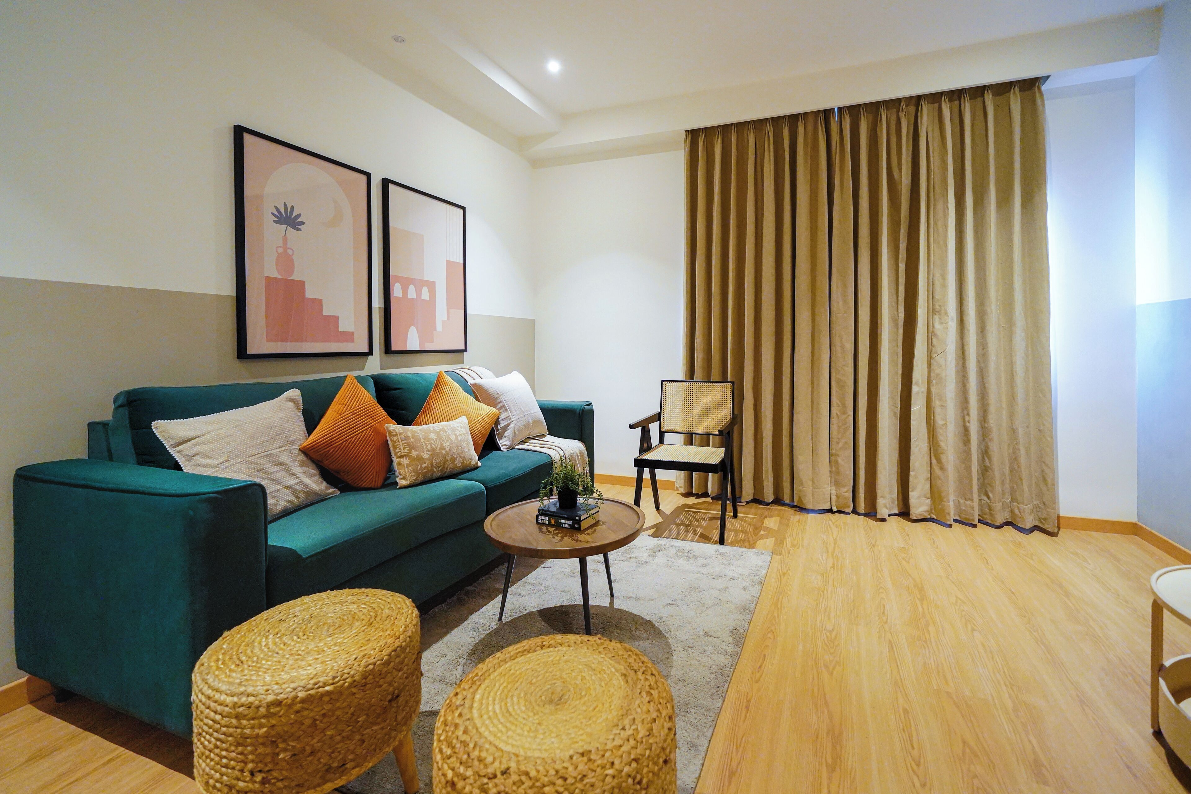 A modern living room with a teal sofa, a coffee table, wicker ottomans, and a large window with curtains.