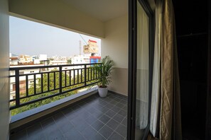 A balcony with a potted plant, a view of buildings, and a curtain. - Olive Hotel Benz Circle, Vijayawada by Embassy Group (Vijayawada)