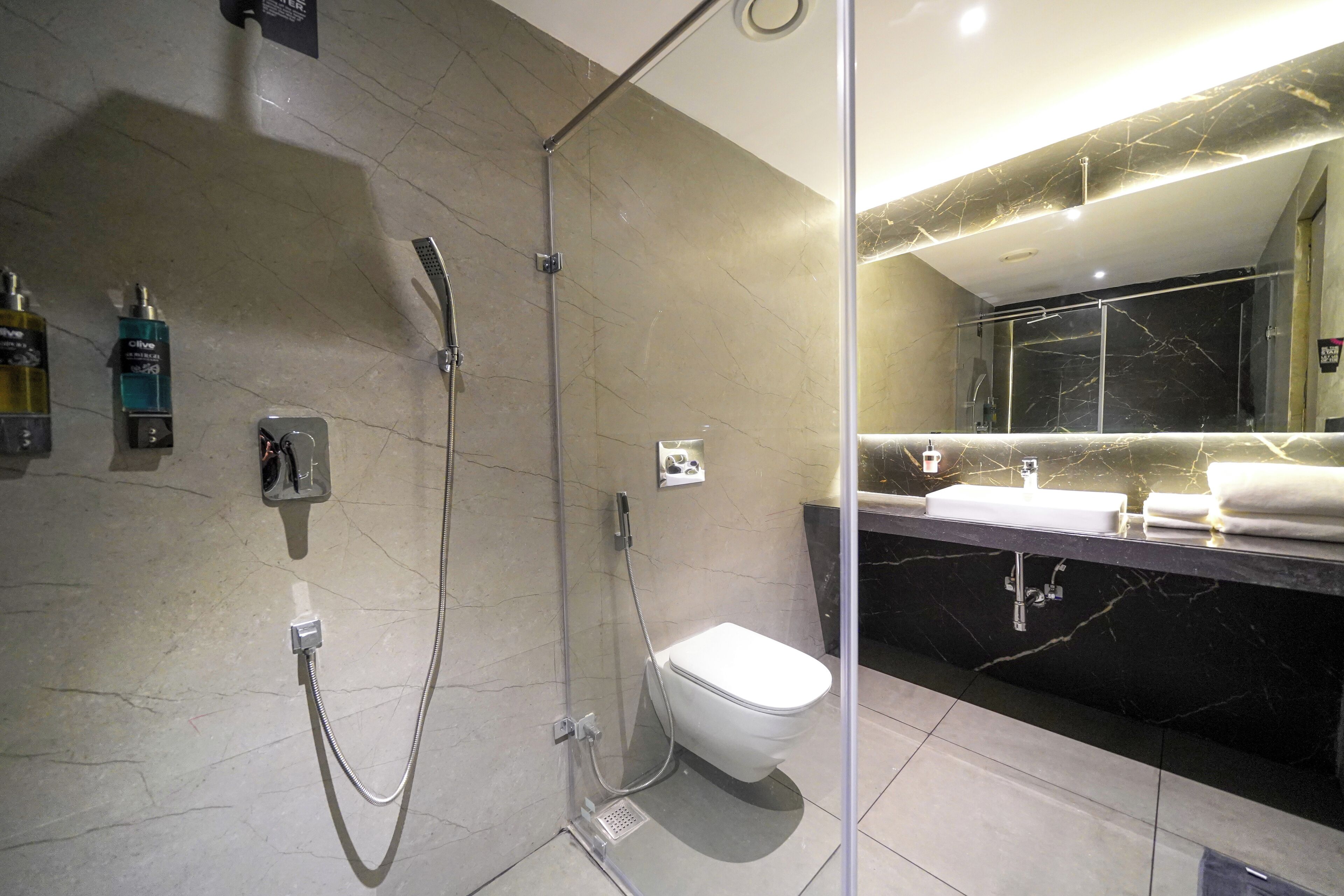 Un baño moderno con ducha envuelta en vidrio, inodoro blanco y tocador de mármol con lavamanos y toalla.