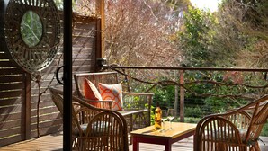 A wooden deck with wicker furniture, a table with wine glasses, and a decorative clock.