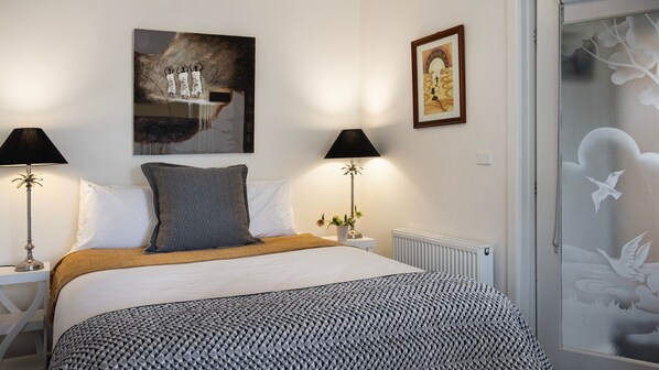A bedroom with a bed, two bedside tables with lamps, a radiator, and artwork on the walls.