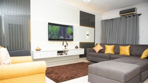 A modern living room with a grey sofa, yellow cushions, a brown rug, and a flat-screen TV mounted on the wall. - Micasa Haven (Lekki)