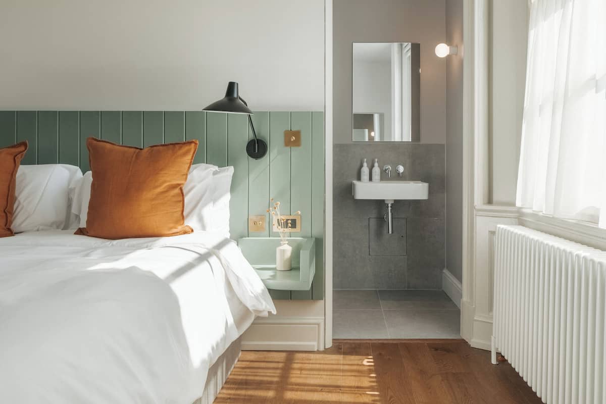 A bedroom with a bed, a bedside table with a lamp, a nightstand, and a view into the bathroom.