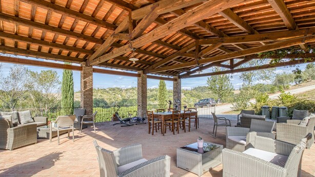 Un patio al aire libre con mobiliario de mimbre, una mesa de madera y vistas al campo.