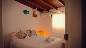 A bedroom with a bed, pillows, a nightstand, a lamp, and a window with curtains. - Posada La Rosaleda (Los Roques)