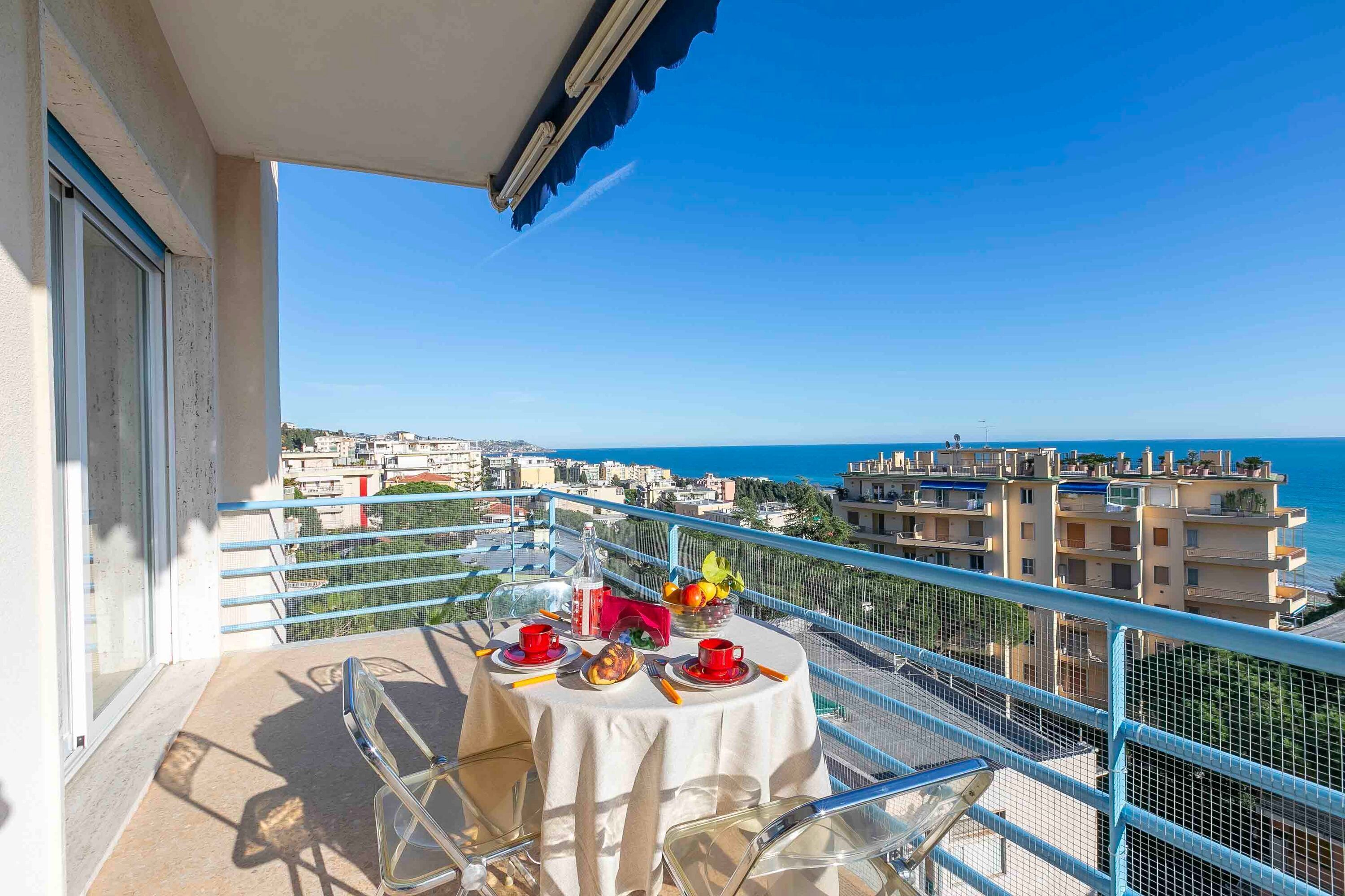 A balcony with a table set for two, overlooking a cityscape and the sea.