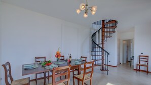 A dining area with a wooden table set for four, surrounded by chairs. A chandelier hangs above, and a spiral staircase is visible in the background. - Palms Villa - Sea View (Sanremo)