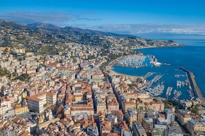 A coastal cityscape with dense urban buildings, a marina, and a mountainous backdrop. - Palms Villa - Sea View (Sanremo)