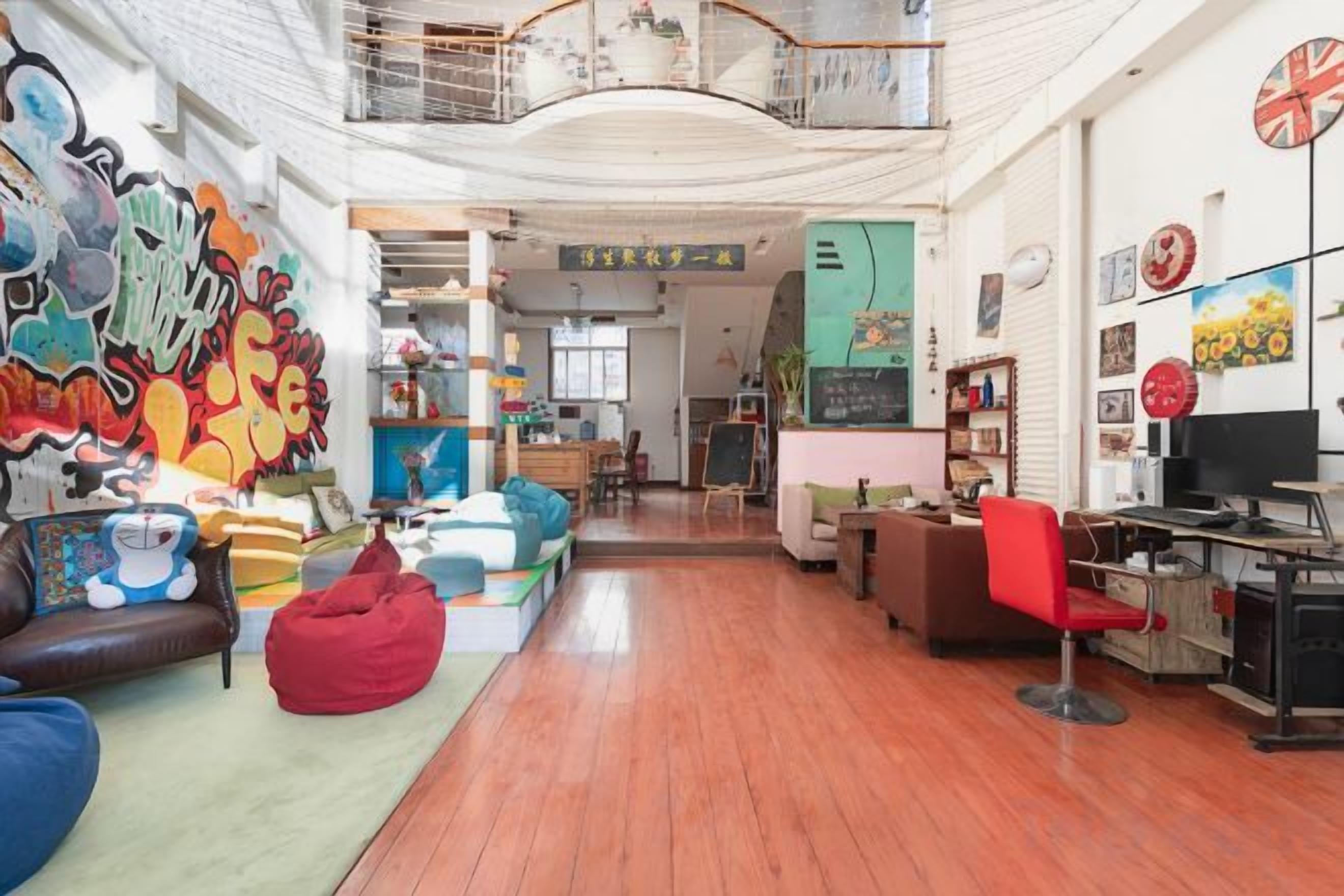 A spacious living area with a high ceiling, a balcony, and a kitchen in the background.
