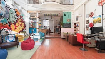A spacious living area with a high ceiling, a balcony, and a kitchen in the background.
