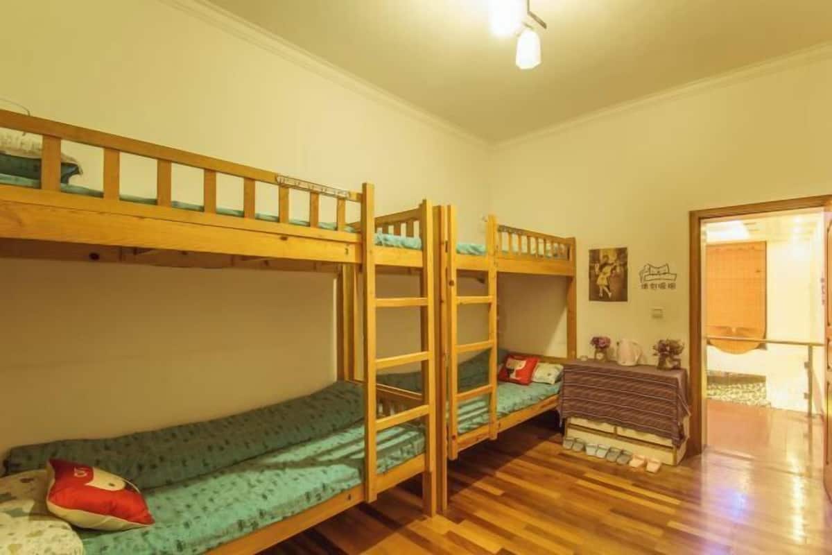 A room with bunk beds, a wooden floor, and a door leading to another room.