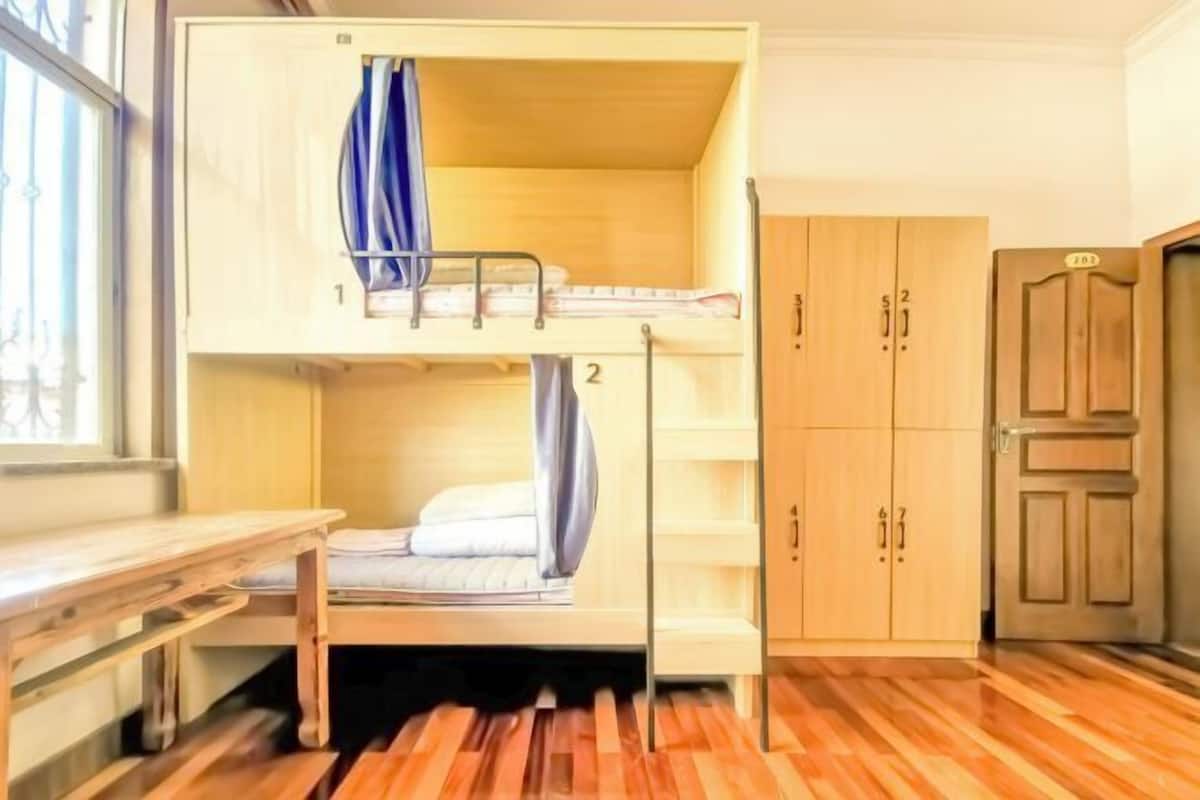 A bunk bed with a desk, wooden wardrobe, and a door with a number.