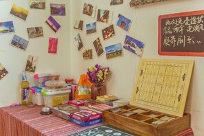 Una habitación con un cofre de madera, una mesa con varios objetos y una pared decorada con fotos y un juego de mesa.