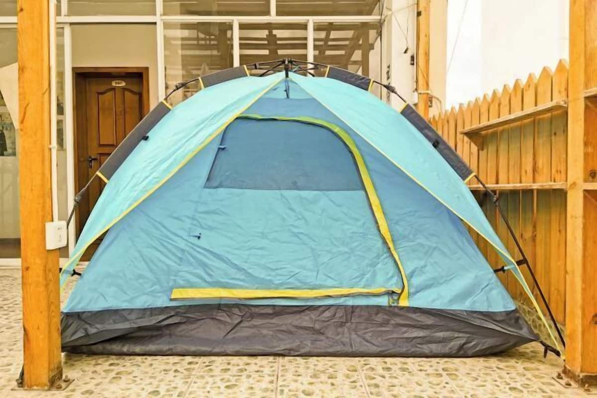 A blue and gray tent set up on a tiled patio with wooden railings and a wooden door in the background.