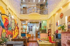 A brightly lit room with a high ceiling, string lights, and a colorful mural on the wall. - Jianying (Lijiang)