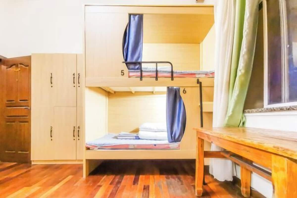 A bunk bed with two levels, wooden cabinets with numbered doors, and a window with curtains.