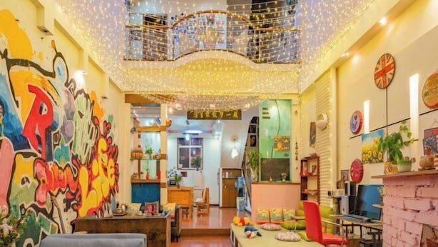 A brightly lit interior with a colorful graffiti wall, a seating area with a table and chairs, and a ceiling adorned with string lights. - Jianying (Lijiang)