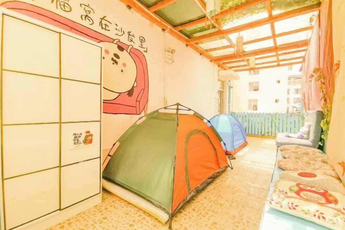 A corridor with a green and orange tent, a sofa with patterned cushions, and a wall with a cartoon character and Japanese text.