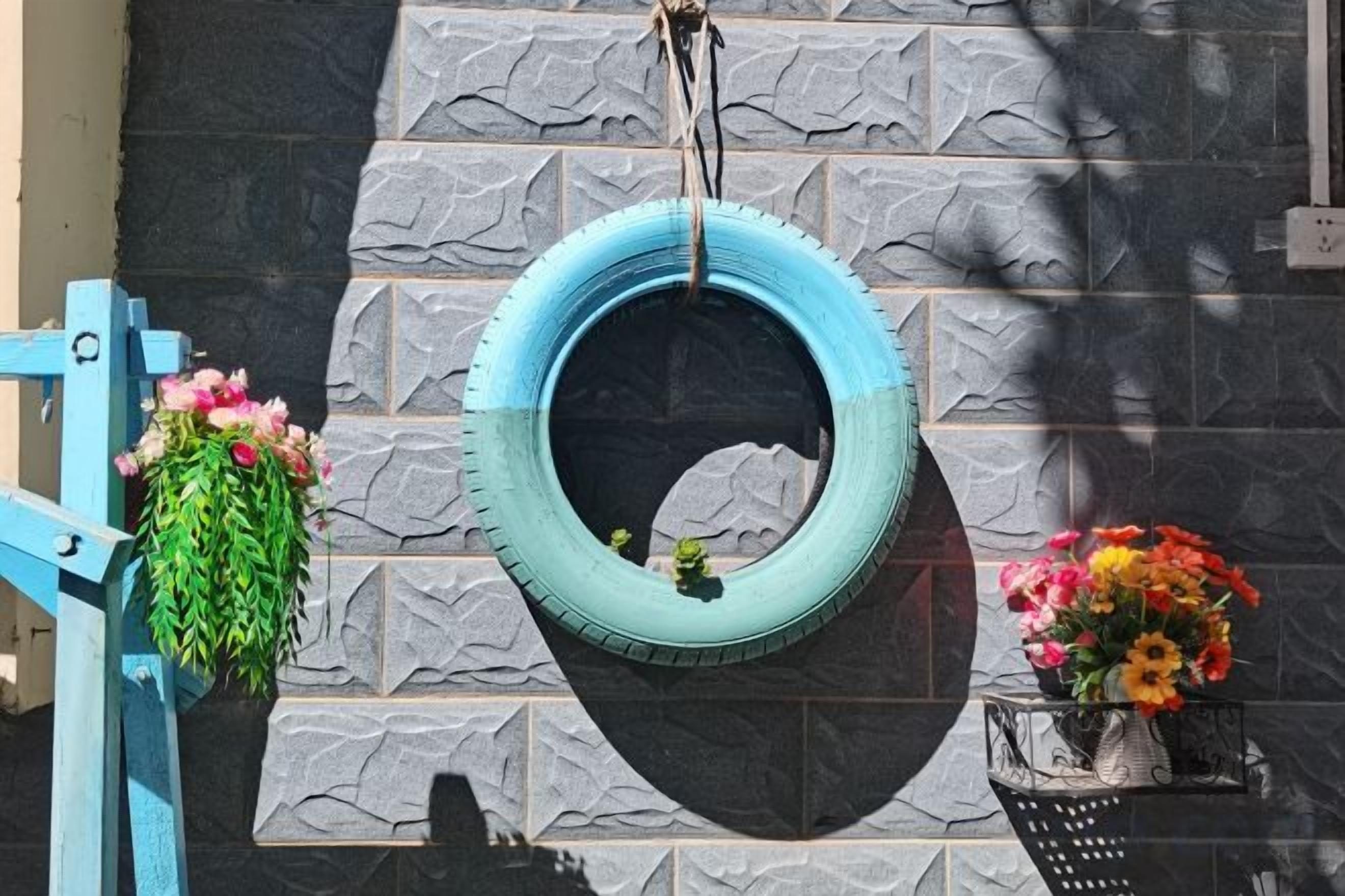 A tire hanging as a planter with flowers, a blue gate, and a wall with a stone pattern.