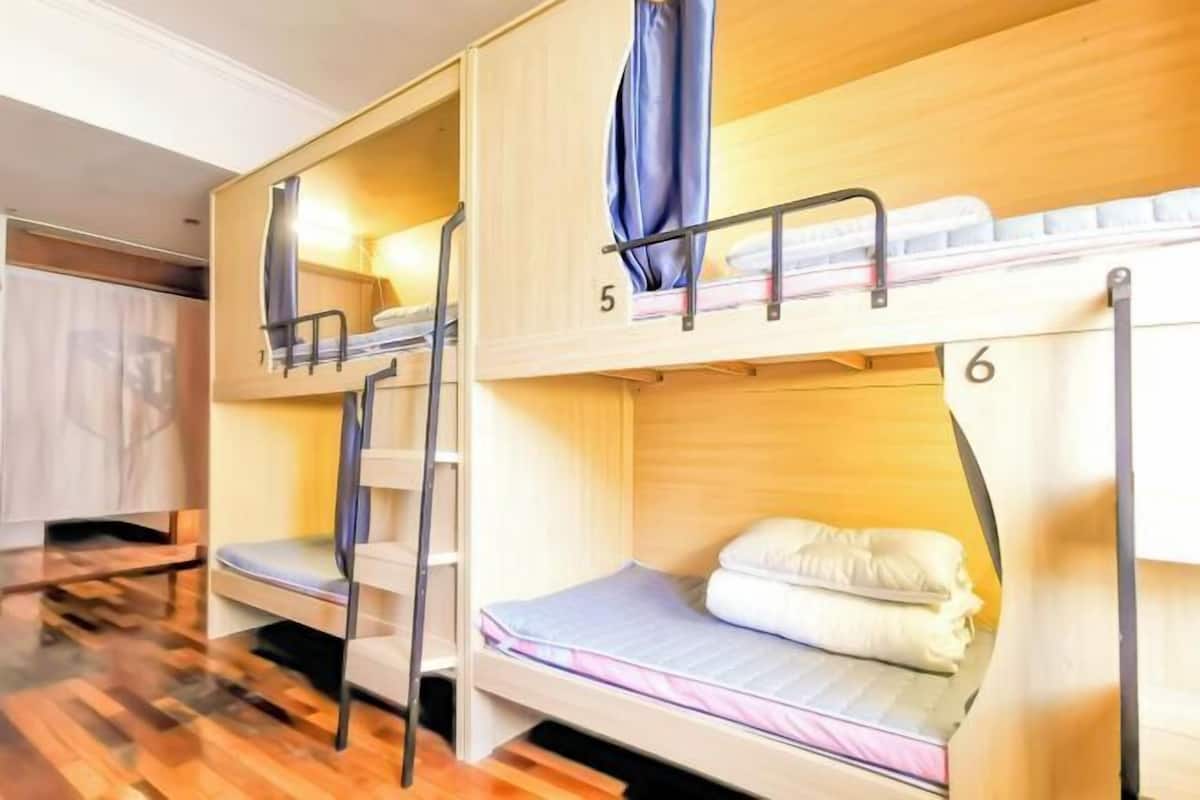 A bunk bed room with two beds, wooden flooring, and a small desk area.