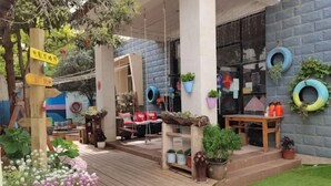A wooden deck with a small garden area, a table with chairs, and a building with a brick facade. - Jianying (Lijiang)