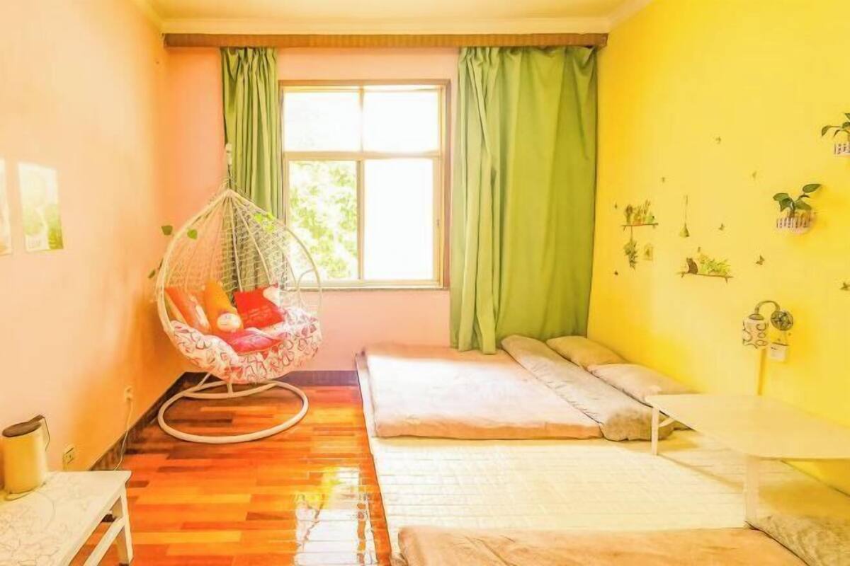 A room with a hanging chair, a bed, a small table, and a window with curtains.
