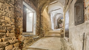 A narrow stone corridor with a cobblestone path, leading to a door with a metal grille. - Casa Rivolte in San Remo (Sanremo)