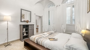 A bedroom with a bed, bedside table, lamp, wardrobe, and a mirror. - Casa Rivolte in San Remo (Sanremo)