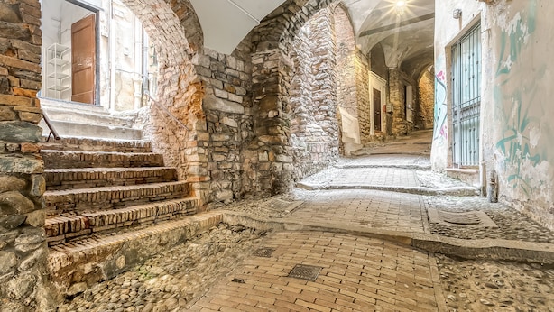 A stone-walled corridor with arched doorways, a brick floor, and a staircase leading to a wooden door. - Casa Rivolte in San Remo (Sanremo)