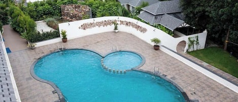 A large, kidney-shaped swimming pool with a stone border, surrounded by a white wall and potted plants.