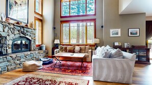 A spacious living room with a stone fireplace, large windows, a sofa, and a coffee table.
