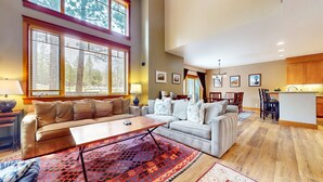 A spacious living room with a large sofa, a coffee table, and a dining area with a kitchen in the background.