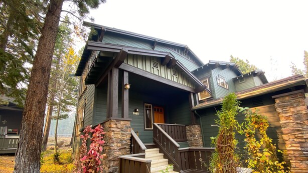 A two-story house with a stone foundation, a wooden porch, and a staircase leading to the entrance.