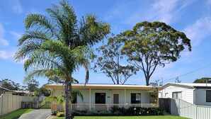 A two-story house with a front porch, a fenced yard, and a large tree. - Clifton Cottage by Experience Jervis Bay (Sanctuary Point)