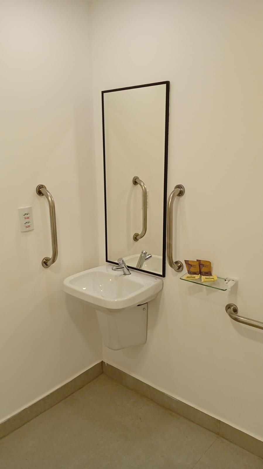 A bathroom with a white sink, a mirror, and two handrails.