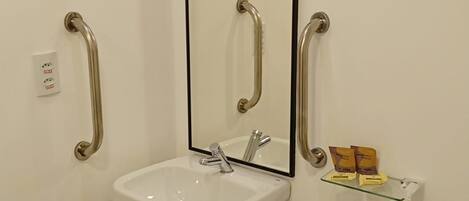 A bathroom with a white sink, a mirror, and two handrails.