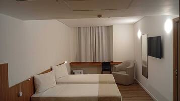A hotel room with two beds, a desk, a chair, a TV, and a window with curtains.