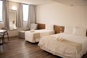 Habitación de hotel con dos camas, una silla, una mesa y un ventanal con cortinas.