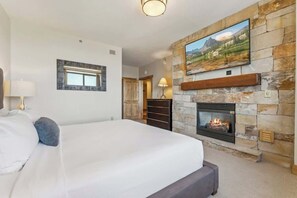 Una camera da letto con camino in pietra, un letto, una TV a muro e una finestra con cornice decorativa.
