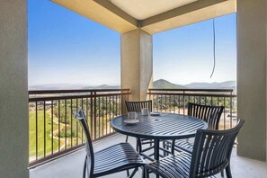 Un balcone con un tavolo rotondo e sedie, che offre vista su un campo da golf e montagne lontane.