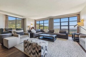 A spacious living room with a large window, a sofa set, a coffee table, and a patterned ottoman. - Ski-In Out Grand Summit Penthouse w Private Sauna (Park City)