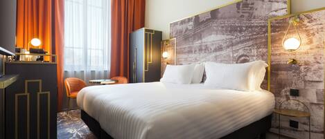 A hotel room with a large bed, a desk with a lamp, a chair, and a wall-mounted TV.