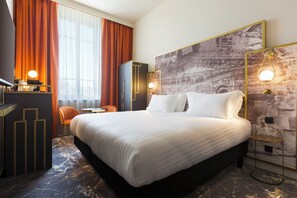 Ein Hotelzimmer mit einem großen Bett, einem Schreibtisch mit Lampe, einem Sessel und einem an der Wand montierten Fernseher.