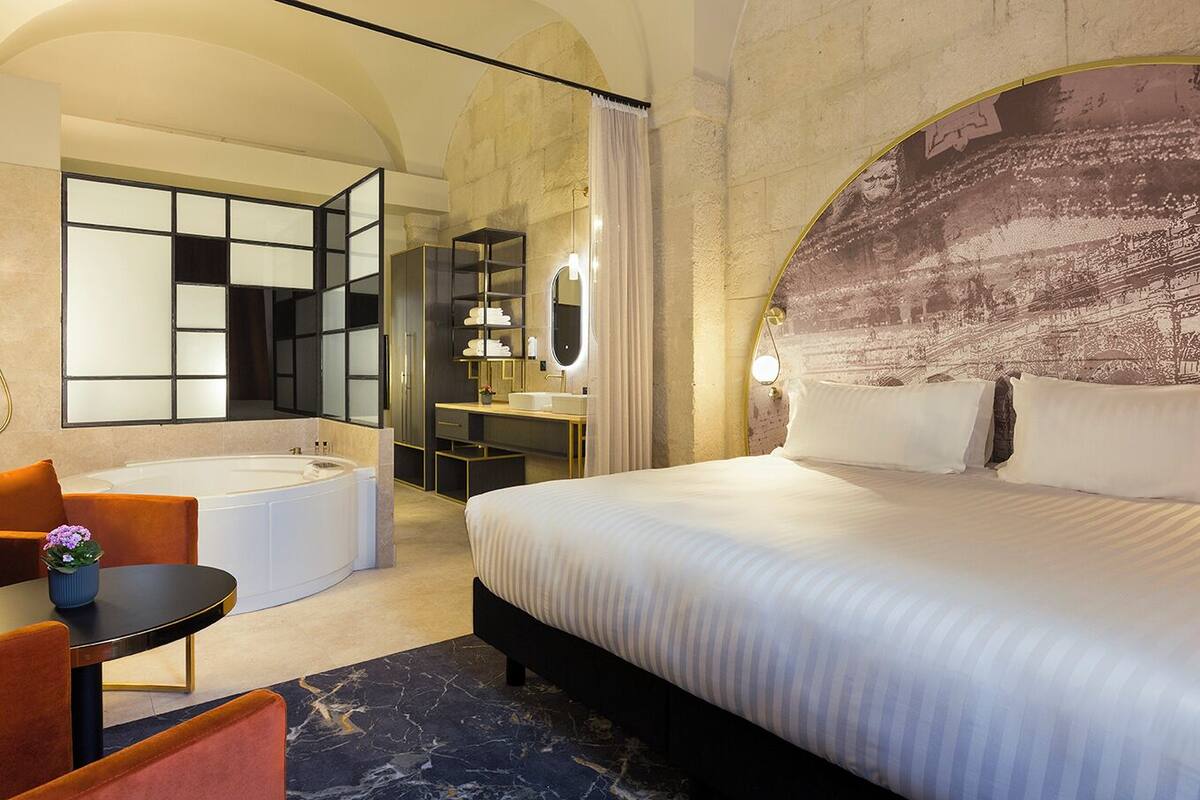 Hotelkamer met een groot bed, een eigen badkamer met ligbad, een bureau met stoel en een klein tafeltje met een plant.