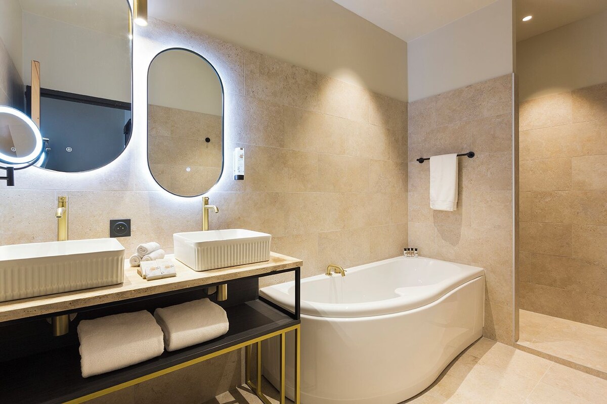Un baño moderno con dos lavamanos, un espejo grande y una bañera independiente.