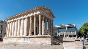 A classical building with columns, a modern glass structure nearby, and a paved area with steps.