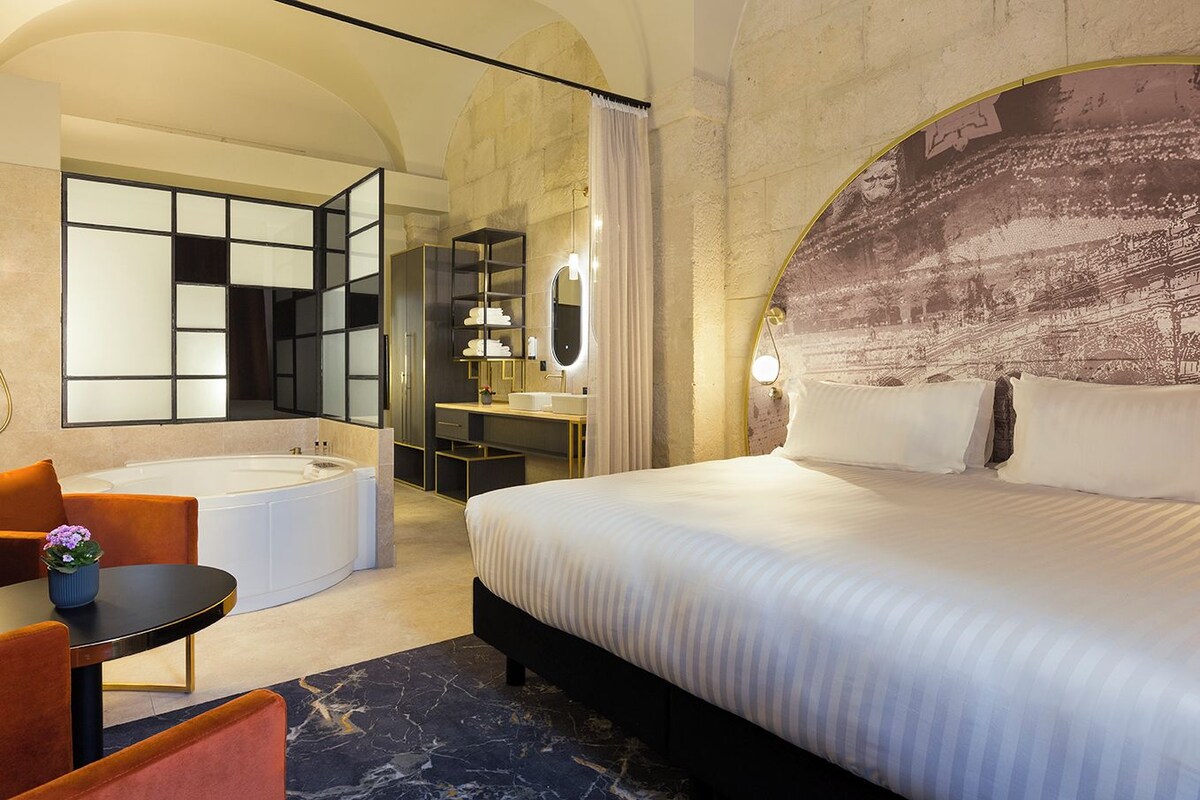Hotelkamer met een groot bed, een eigen badkamer met ligbad, een bureau met stoel en een klein tafeltje met een plant.
