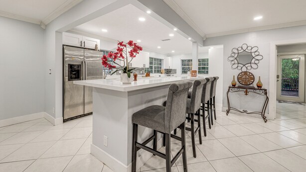 A modern kitchen with a central island, bar stools, a refrigerator, and a decorative mirror. - Boca Raton Home: Outdoor Kitchen, By Golf Courses (Boca Raton)